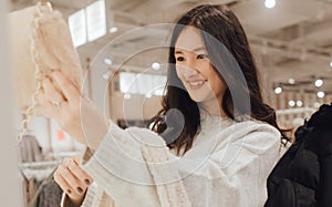 Korean teenage girl choosing and buying trendy clothes in a shopping mall. Retail and consumerism. Sale promotion and shopping