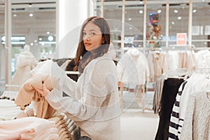 Korean teenage girl choosing and buying trendy clothes in a shopping mall. Retail and consumerism. Sale promotion and shopping