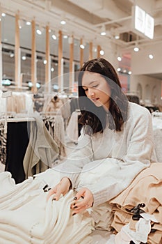 Korean teenage girl choosing and buying trendy clothes in a shopping mall. Retail and consumerism. Sale promotion and shopping