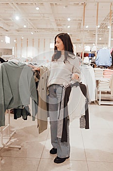 Korean teenage girl choosing and buying trendy clothes in a shopping mall. Retail and consumerism. Sale promotion and shopping