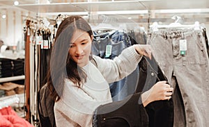 Korean teenage girl choosing and buying trendy clothes in a shopping mall. Retail and consumerism. Sale promotion and shopping