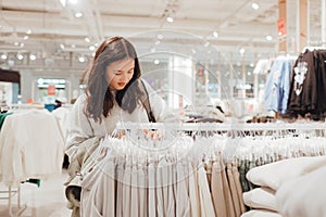 Korean teenage girl choosing and buying trendy clothes in a shopping mall. Retail and consumerism. Sale promotion and shopping