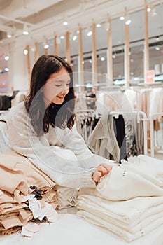 Korean teenage girl choosing and buying trendy clothes in a shopping mall. Retail and consumerism. Sale promotion and shopping