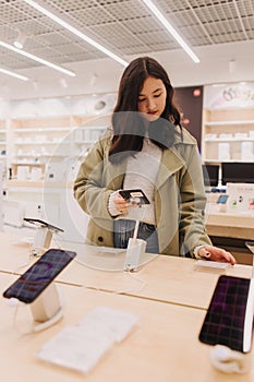 Korean teenage girl choosing phone at technology store. Female customer viewing smart phones in store. Retail and consumerism.