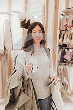 Korean teenage girl holds a credit card in her hands and wants to pay for new clothes in a shopping mall. Retail and consumerism.