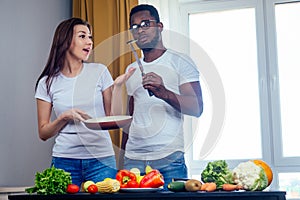 Korean woman wearimg white cotton t-shirt with her african american boyfriend cooking in fry pan bresksast