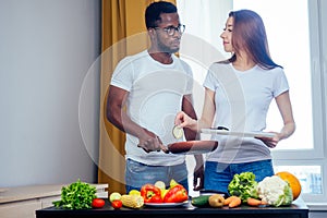 Korean woman wearimg white cotton t-shirt with her african american boyfriend cooking in fry pan bresksast