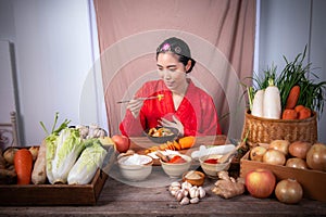 A Korean woman wears a traditional hanbok. She makes kimchi. ?