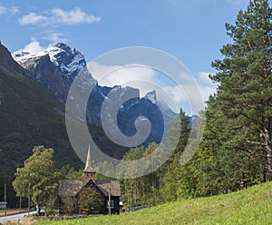 Kors Church, old wooden parish church in Rauma in Romsdal valley, Norway with road E136, green forest and mountain