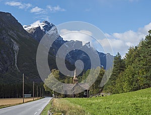 Kors Church, old wooden parish church in Rauma in Romsdal valley, Norway with road E136, green forest and mountain massif