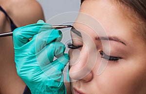 Kosmetolog- makeup artist applies paint henna on previously plucked, design, trimmed eyebrows in a beauty salon