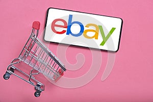 Kostanay, Kazakhstan, August 31, 2023.Smartphone with ebay logo,shopping basket pink background.Concept online shopping.