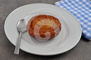 Kouign-amann in a plate with a spoon close-up on a gray background