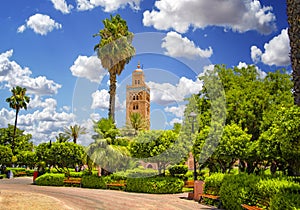 Koutoubia Mosque minaret at medina quarter of Marrakesh, Morocco. There is beautiful green garden with palms. Blue sky is in the
