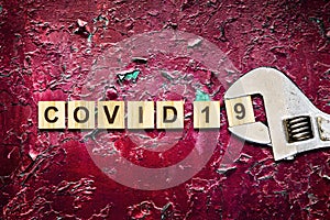 KOVID 19. The inscription on the wooden blocks and the adjustable wrench on the background of a red cracked wall. The concept of