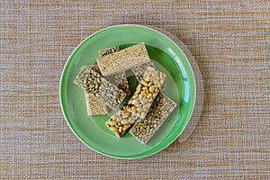 Kozinaki with seeds, nuts, sesame seeds with honey in a green plate, on a brown mat. Useful snacks. Fitness nutrition, nutritious
