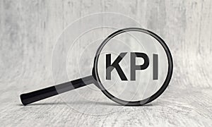 KPI acronym, word through magnifier on wooden background