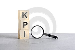 KPI - Key Performance Indicators - text on wooden cube blocks and magnifying glass on grey table