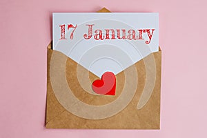 Kraft envelope with a white sheet of paper and a date 17 january, with a red heart. Flat lay on pink background, romance and love