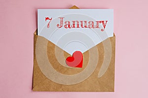 Kraft envelope with a white sheet of paper and a date 7 january, with a red heart. Flat lay on pink background, romance and love