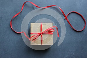 Kraft gift box with red ribbon on textured black vintage background