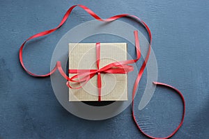 Kraft gift box with red ribbon on textured black vintage background