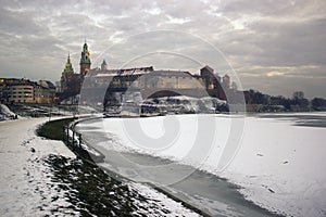 Krakow, Poland : Wide angle view of famous wawel castle covered with snow next to vistual river against dramatic