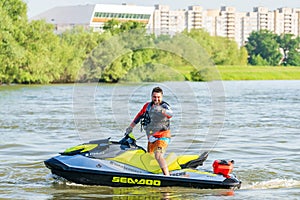 Happy smiling man on BRP Sea-Doo jet ski showing thumb up at sunset by river bank at countryside. Extreme sports and active summer