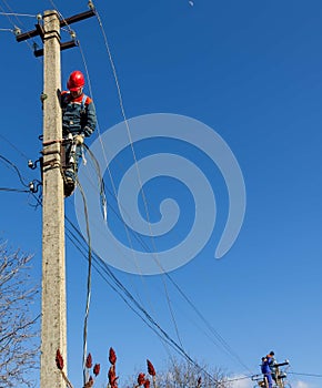 Male electricians on poles mount a new line of electrical wires against a blue sky with a copy space
