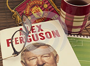 Reading autobiography book by Alex Ferguson, a football coach. Glasses, sports pennant