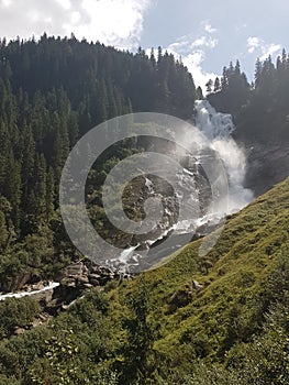 Krimml waterfall Austria rushing water with extreme power surrounded by tall green trees and blue bright sky