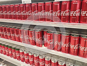 Soft drinks in cans are displayed on a shelf for sale in a large supermarket.