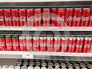 Soft drinks in cans are displayed on a shelf for sale in a large supermarket.