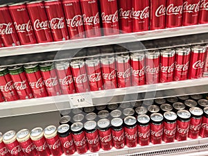 Soft drinks in cans are displayed on a shelf for sale in a large supermarket.