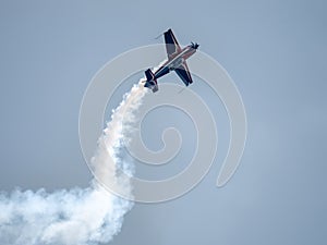 Silhouette of an airplane with trail of smoke behind against background of blue sky.