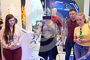 KUBINKA, RUSSIA, AUG.24, 2018: Young girl in exosuit and virtual reality glasses is trying to operate space robot on a computer si