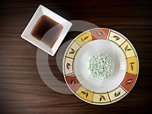 Kuih Lopes is on a round plate with a diamond-shaped sweet sauce on the side, wooden  background.