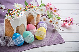 Kulich, traditional Russian Ukrainian Easter cake with icing and colored eggs with lace ribbon on white wooden background