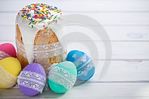 Kulich, traditional Russian Ukrainian Easter cake with icing and colored eggs with lace ribbon on white wooden background with flo