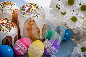 Kulich, traditional Russian Ukrainian Easter cake with icing and colored eggs with lace ribbon on white wooden background