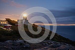 Kullen lighthouse shining its light after sunset. Denmark and sweden in the background