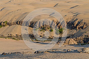 Kunene River in front of towering ancient Namib Desert sand dunes of Namibia and Angola