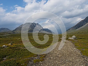 Kungsleden hiking trail path with red marked stones in beautiful wild Lapland nature landscape with green bushes and mountains.