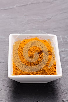 Kurkuma spice powder in white bowl on dark slate background.