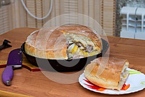 Kurnik, Russian meat pie. A traditional home-made pastry dish lies in a black pan on the table. Neer to a piece of pie on a plate