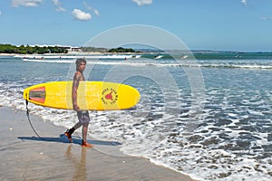 Kuta Beach in Kuta, Bali, Indonesia with a Surfer carrying a Surfboard