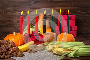 Kwanzaa holiday concept with candles red, black and green, gift box, pumpkins, ears of wheat, grapes, corns, banana, bowl and photo