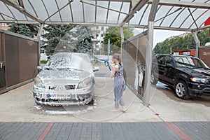 Kyiv, Ukraine- May 15, 2019 Young woman with bucket and rag washing red car