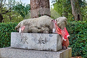 The stone  statue of lying ox  in the red bib at Kitano Tenmangu shrine. Kyoto. Japan