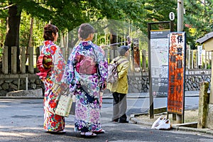 Two female tourists in traditional colorful  japanese kimono taking photo with a selfie stick in front of the bus stop in Kyoto.